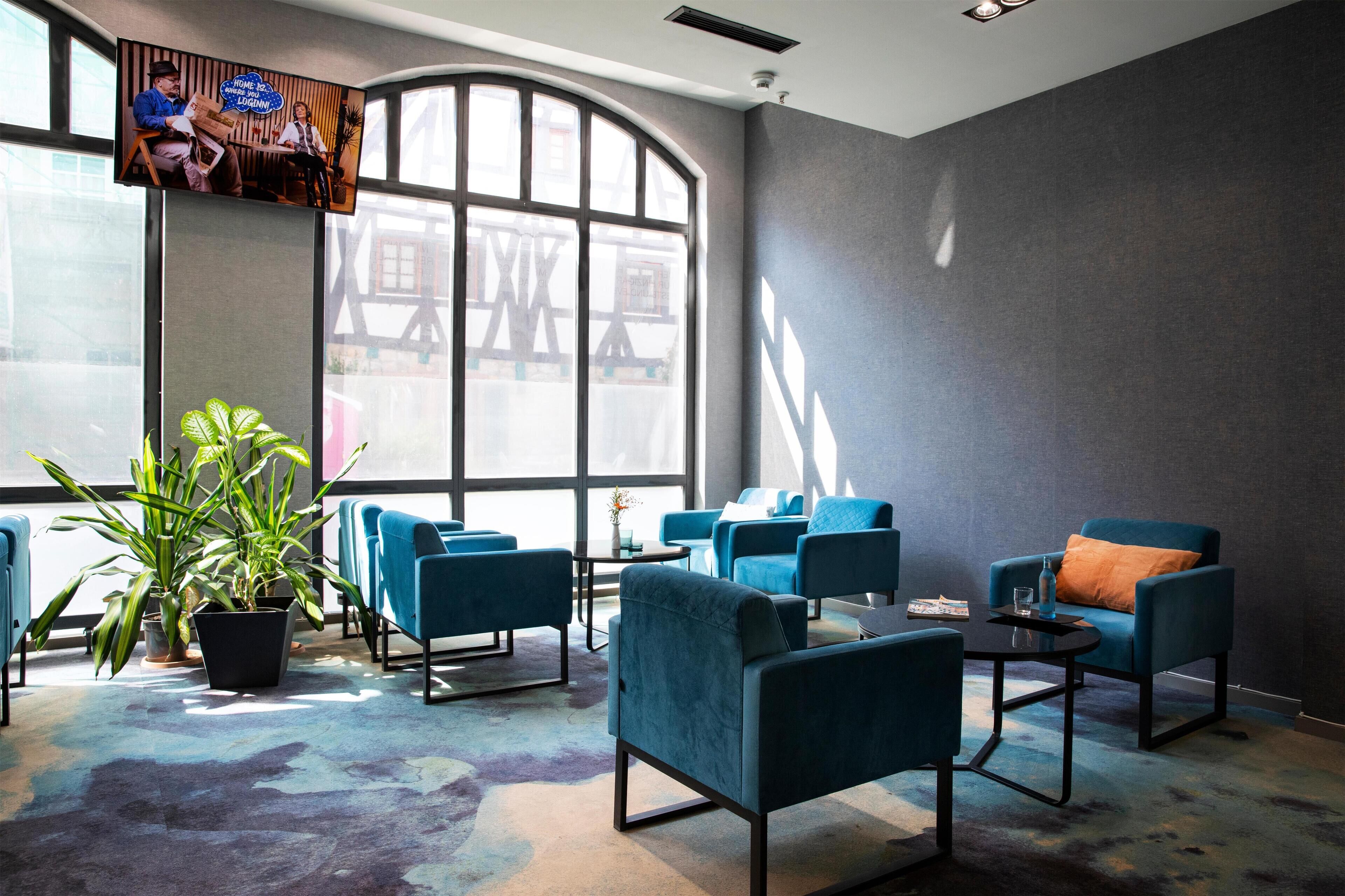 Un área de descanso moderna con sillones azules, una mesa de centro y un ventanal que proporciona luz natural.