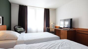 Quarto de hotel com duas camas, uma escrivaninha, uma cadeira, televisão e janela com cortinas.