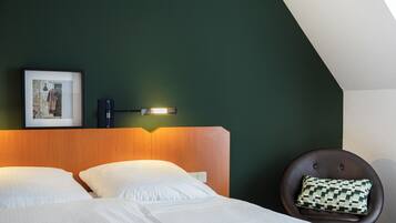 A hotel room with a bed, a chair, a wall-mounted light, and a framed picture.