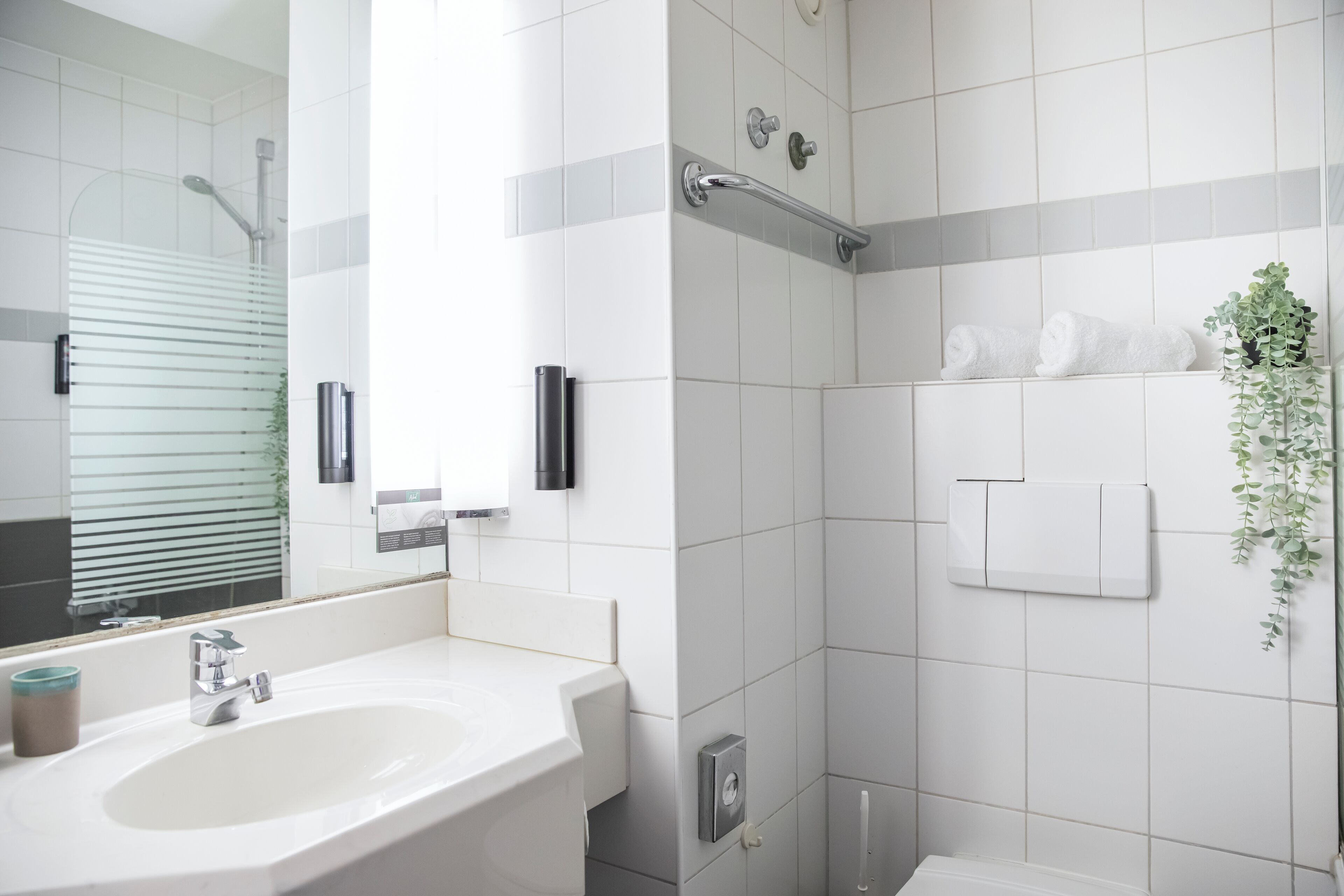 A modern bathroom with a white sink, a mirror, a shower, and a towel rack.
