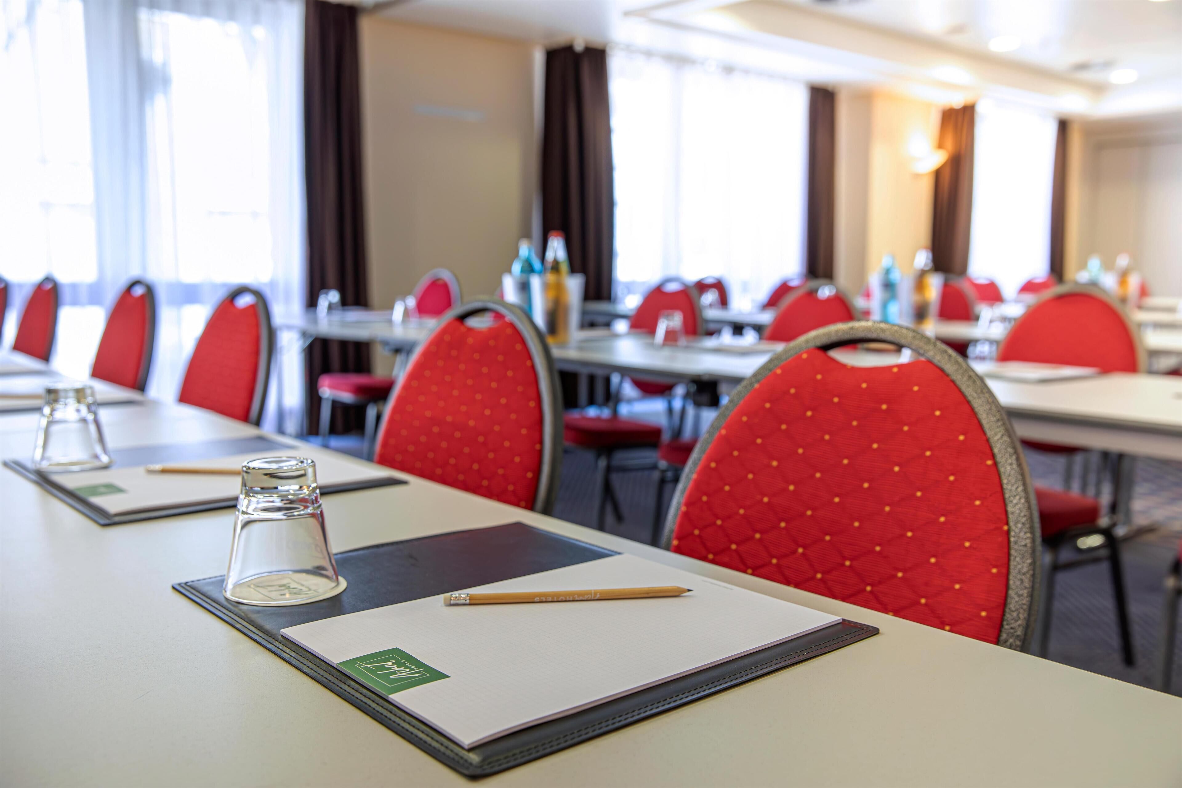 Une salle de conférence avec des chaises rouges, une table sur laquelle se trouvent un verre, un bloc-notes et un crayon.