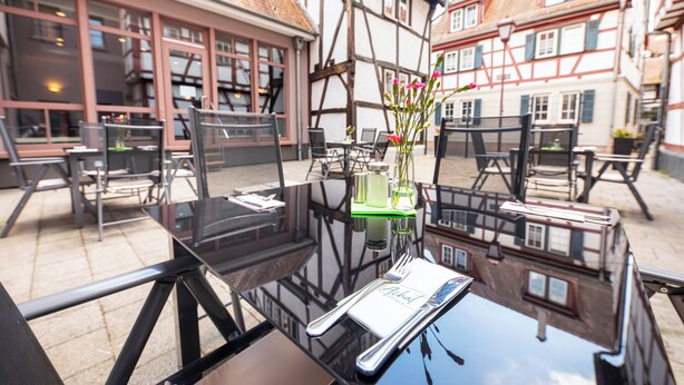 An outdoor dining area with tables and chairs, a vase with flowers, and a menu on a glass table. - ACHAT Hotel Heppenheim (Heppenheim)