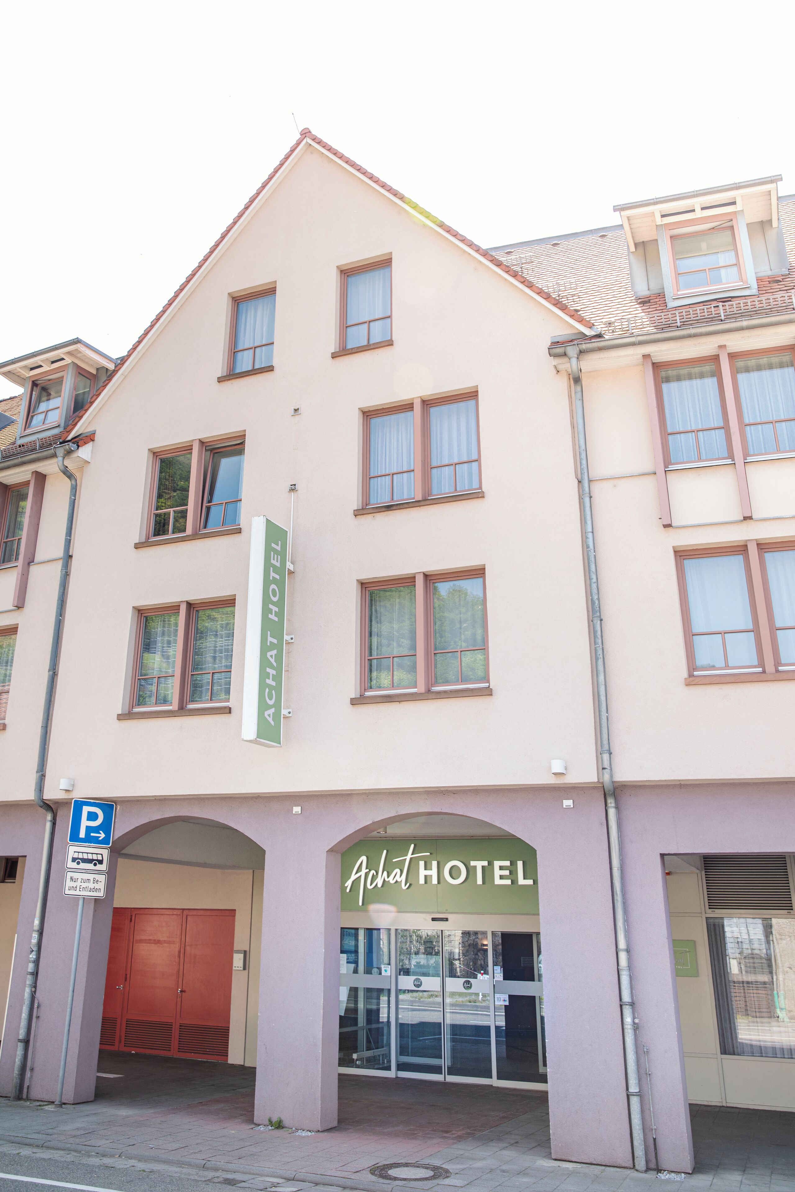 Un hotel con un cartel que dice "Achat Hotel" y un letrero que indica una zona de estacionamiento para autobuses y taxis.