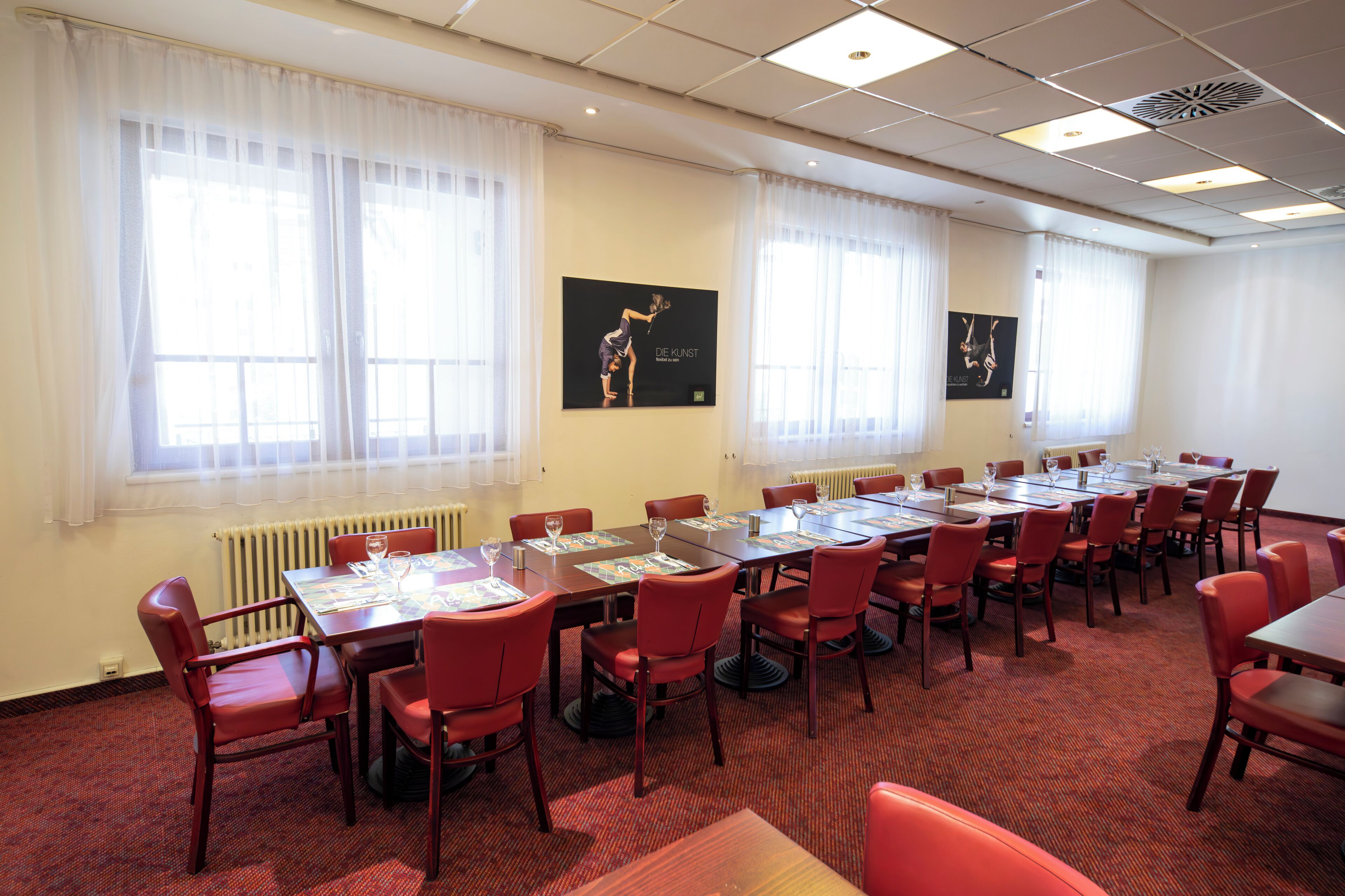 Une salle de conférence dotée de plusieurs tables et chaises, de grandes fenêtres avec des rideaux légers et d’œuvres d’art accrochées aux murs.