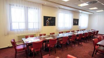 Une salle de conférence dotée de plusieurs tables et chaises, de grandes fenêtres avec des rideaux légers et d’œuvres d’art accrochées aux murs.
