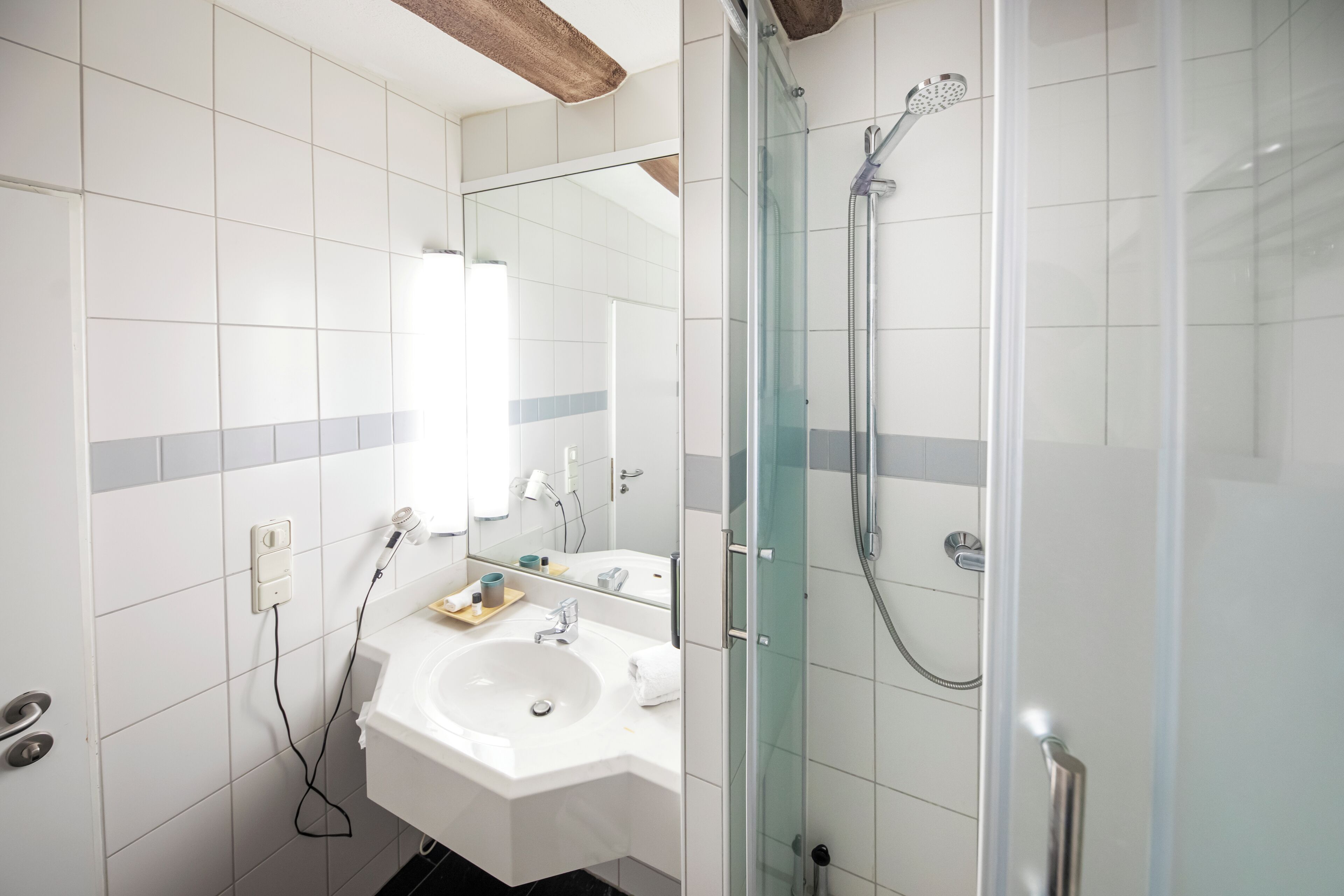 Een moderne badkamer met een douchecabine van glas, een witte wastafel en een spiegel erboven.