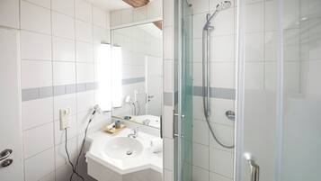 Een moderne badkamer met een douchecabine van glas, een witte wastafel en een spiegel erboven.