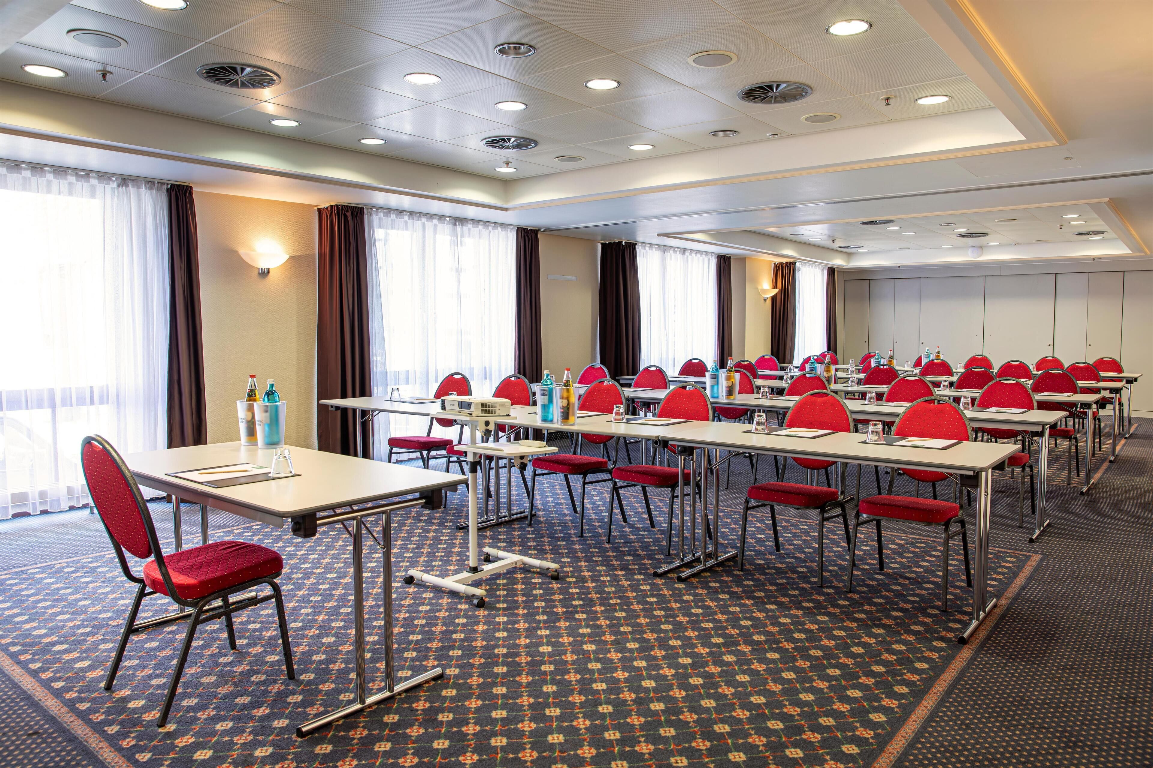 A conference room with multiple tables and red chairs, equipped with water bottles and a projector.