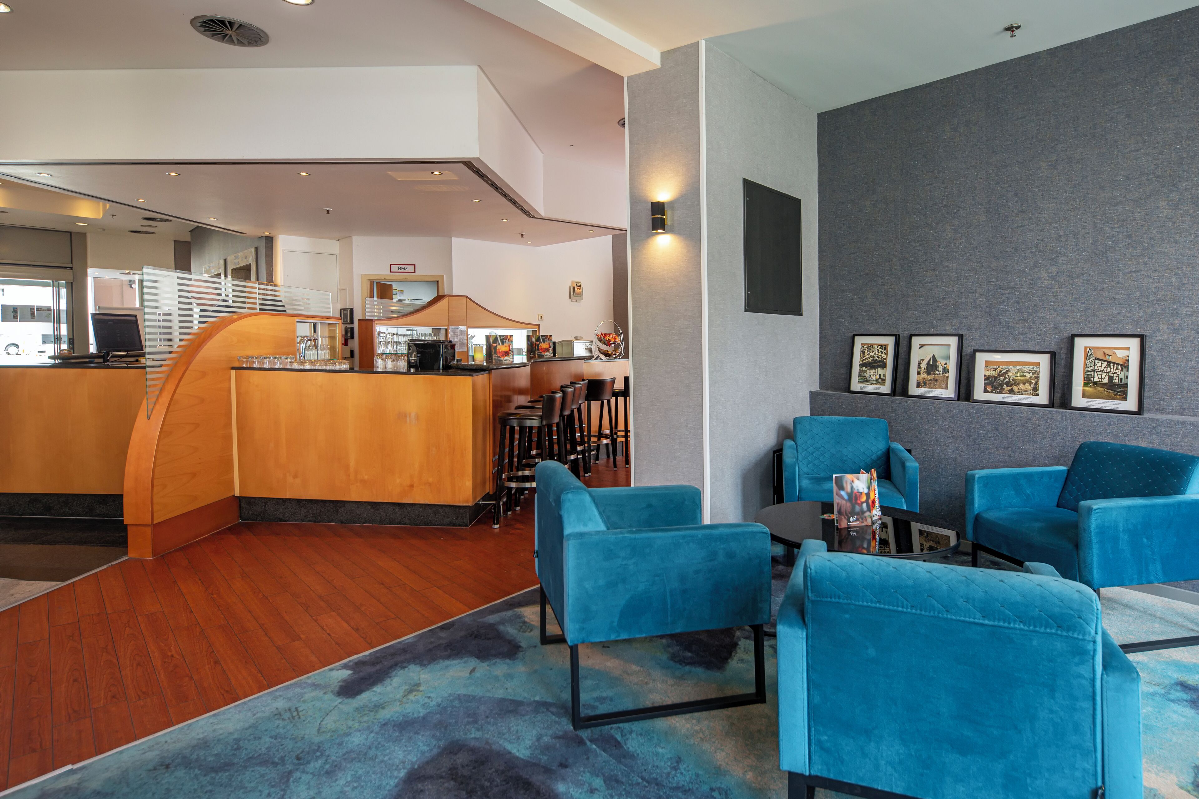 A hotel lobby with a reception desk, blue seating area, and framed pictures on the wall.