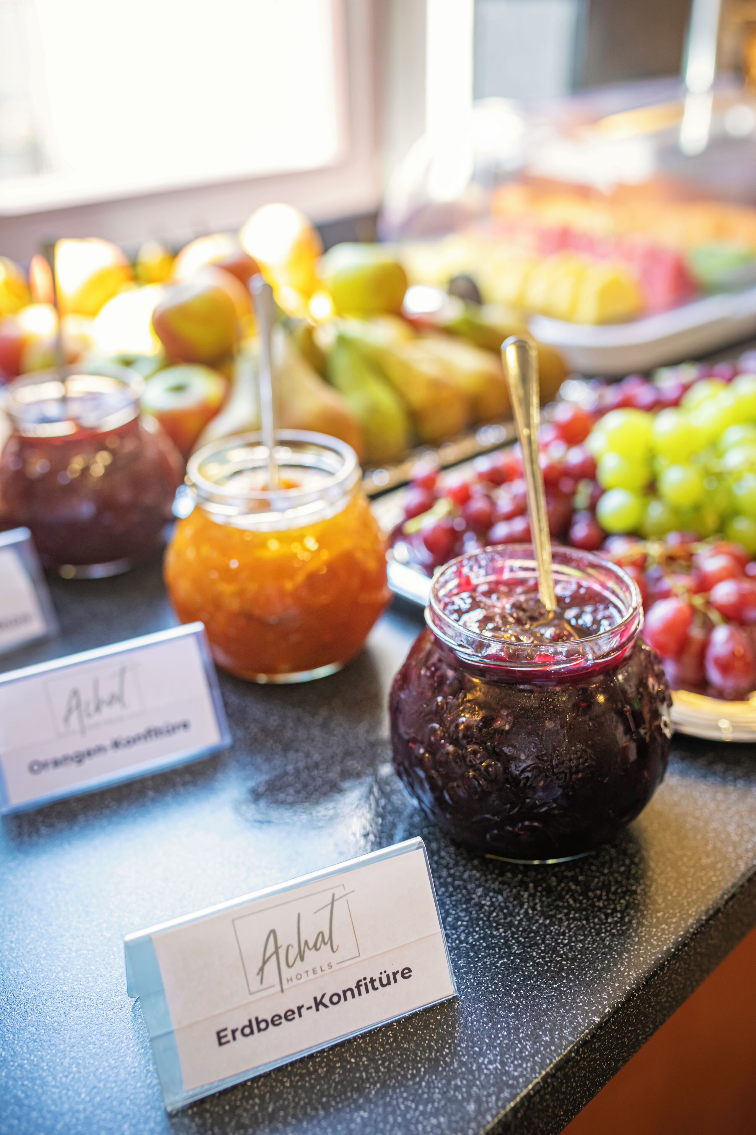 A buffet table with various fruits and jams, including apples, grapes, and jars of preserves.