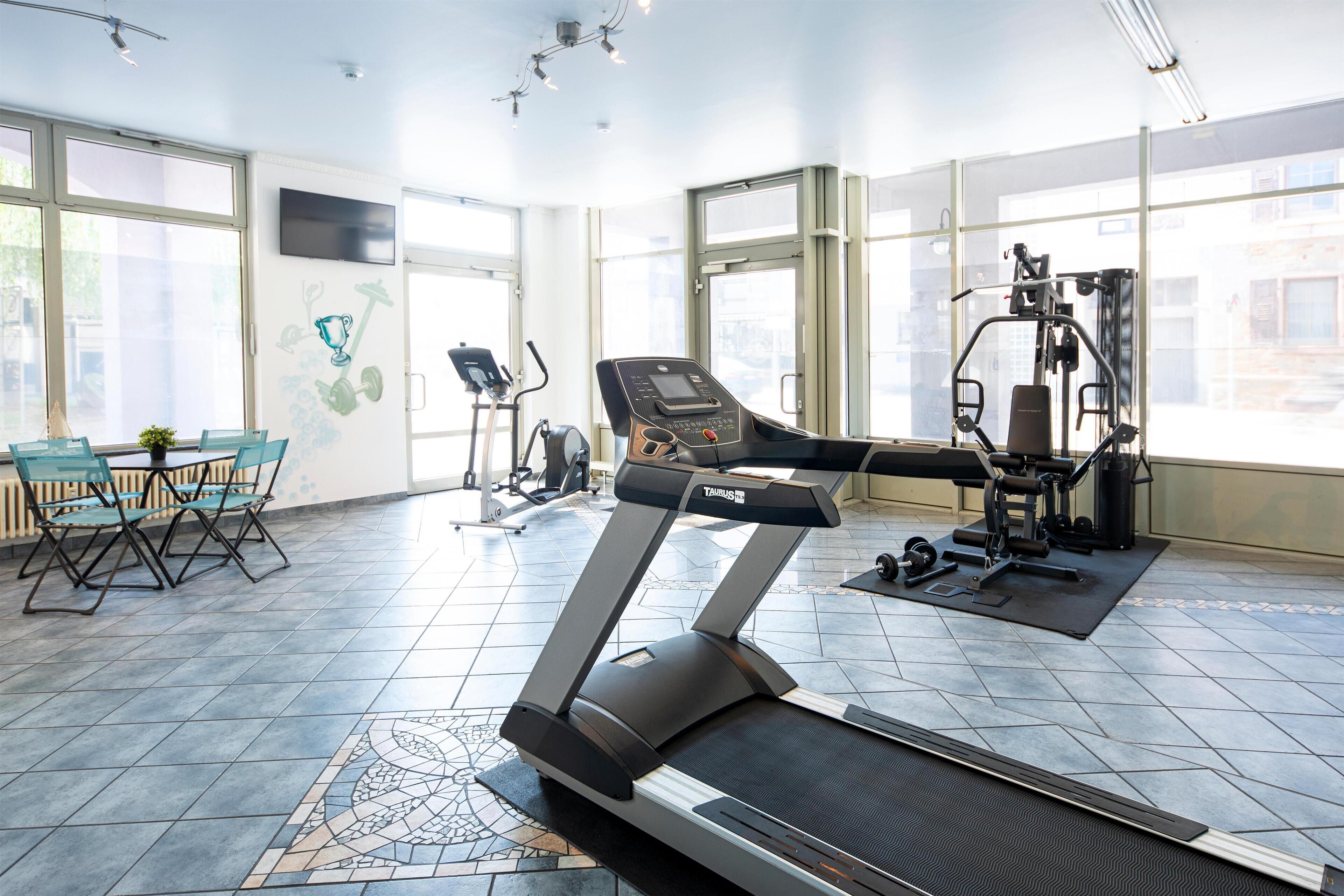Un gimnasio con cinta de correr, máquinas de ejercicio y un comedor con sillas.