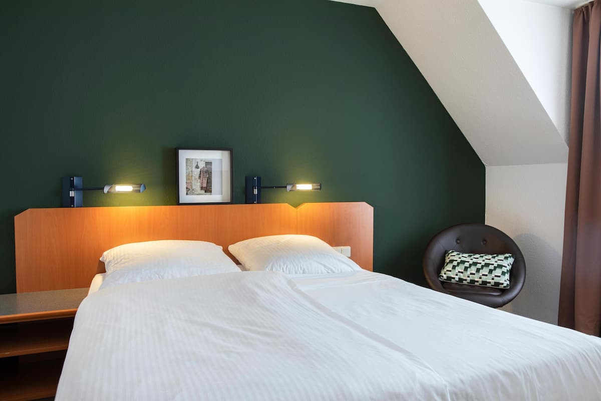 A neatly made bed with white linens, a wooden headboard, and two wall-mounted reading lamps.