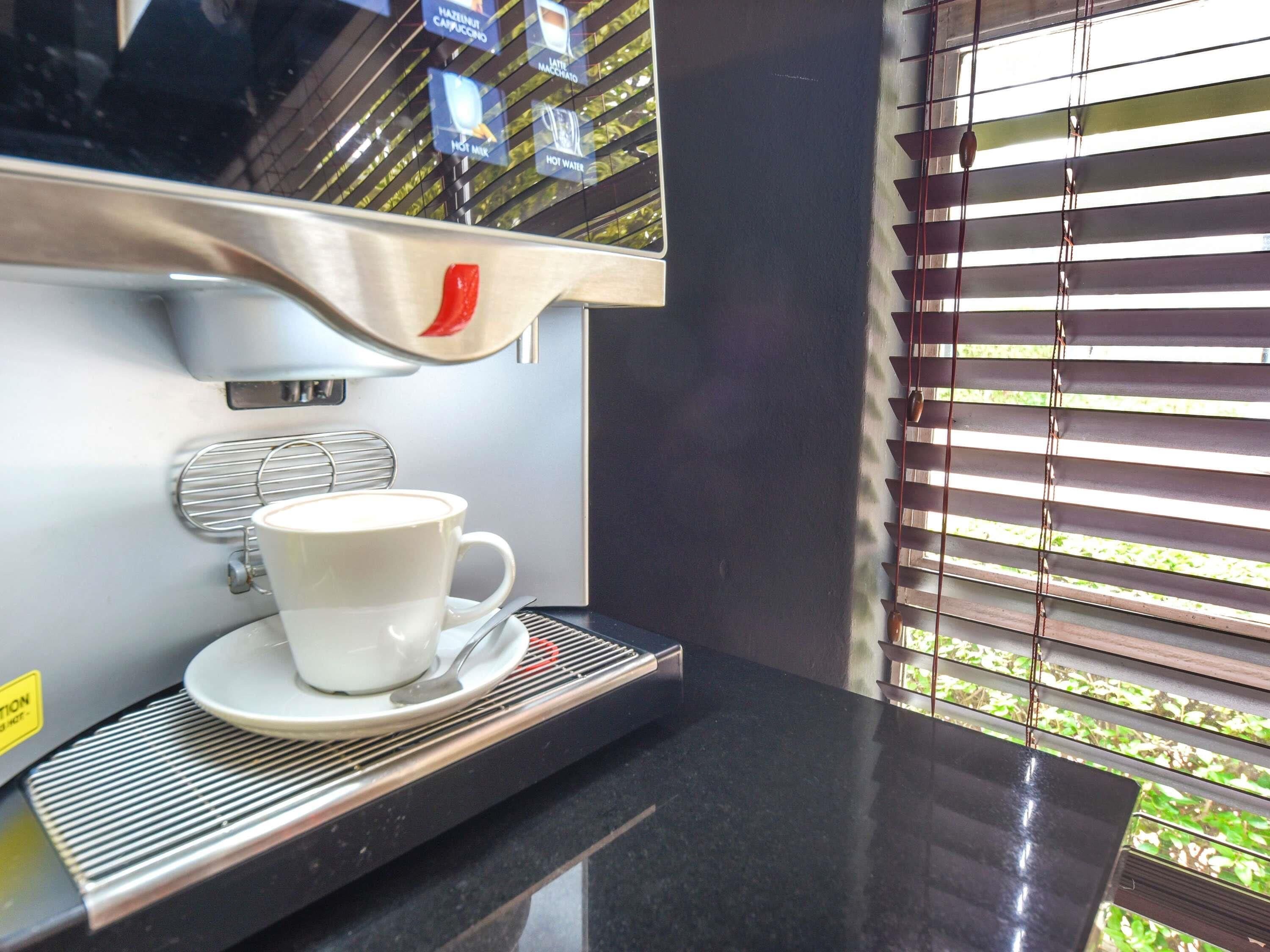 A coffee machine with a cup and saucer, a window with blinds, and a metal grate.