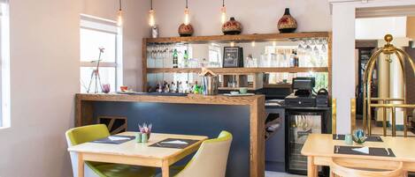 A restaurant with a bar area, wooden furniture, and hanging pendant lights.