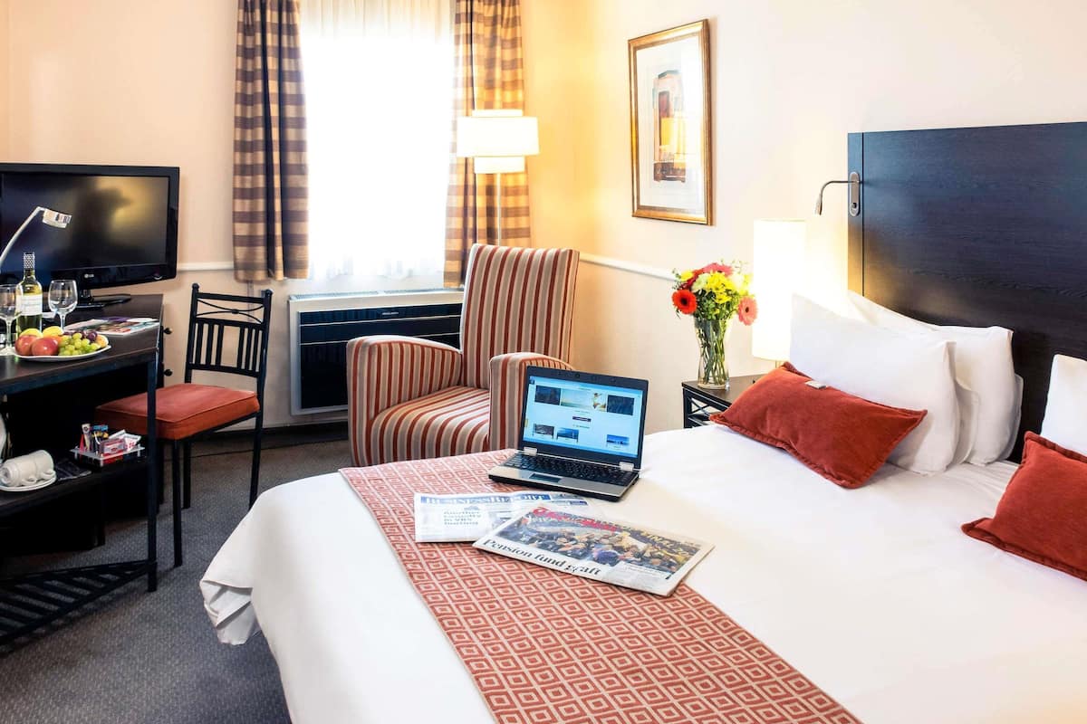 A hotel room with a bed, a desk with a laptop, a television, and a chair.