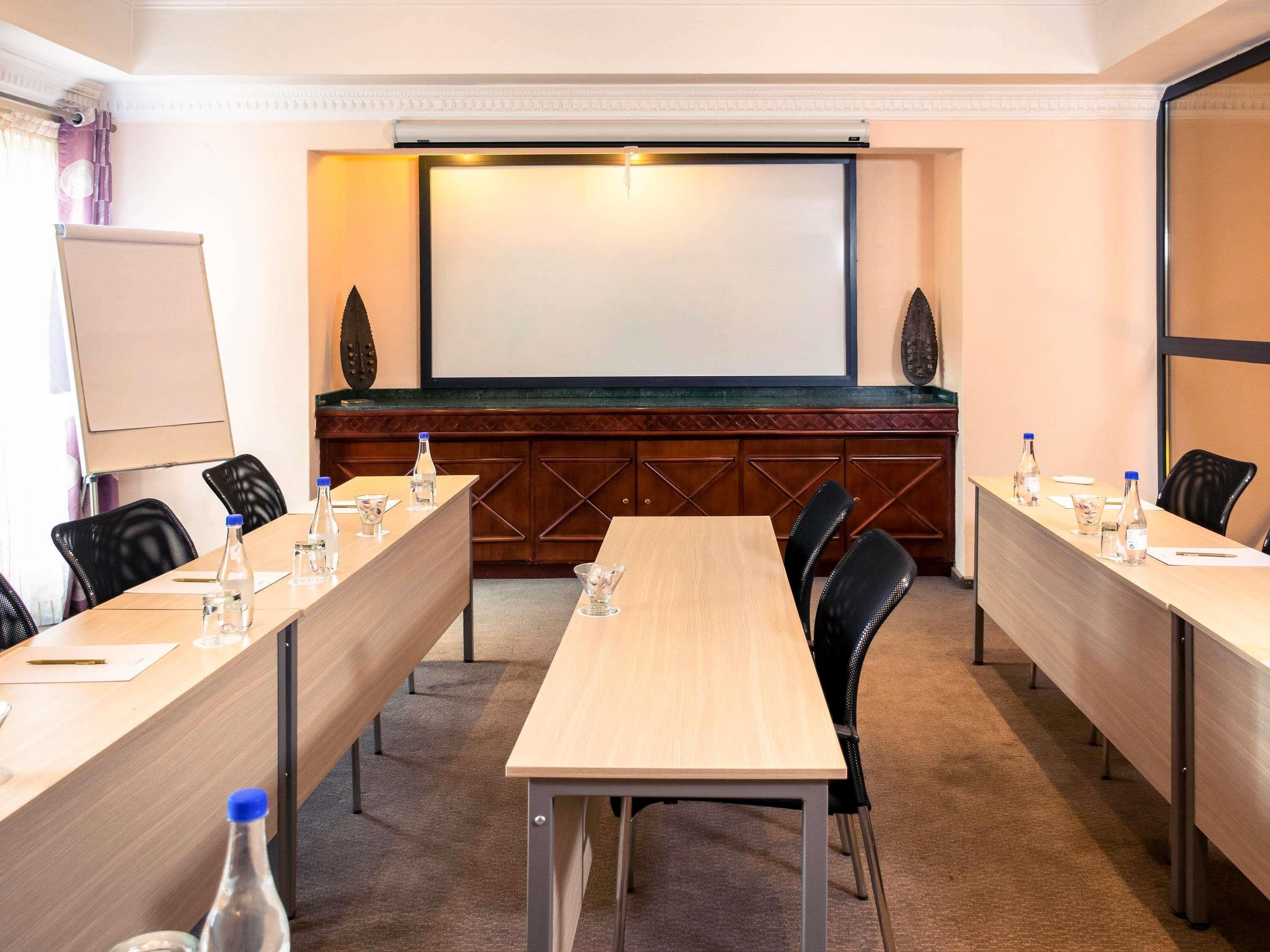 Una sala de conferencias con una larga mesa, sillas, una pantalla de proyector y una pizarra.