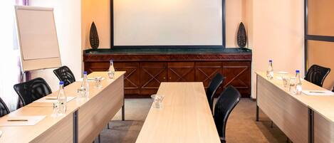 Una sala de conferencias con una larga mesa, sillas, una pantalla de proyector y una pizarra.