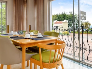 A hotel dining area with tables set for two, chairs with green cushions, and a view of the hotel and surroundings through large windows. - Mercure Johannesburg Midrand Hotel (Midrand)