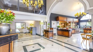 A spacious lobby with a high ceiling, a central island with a kitchen area, and a reception desk with a vase of flowers.