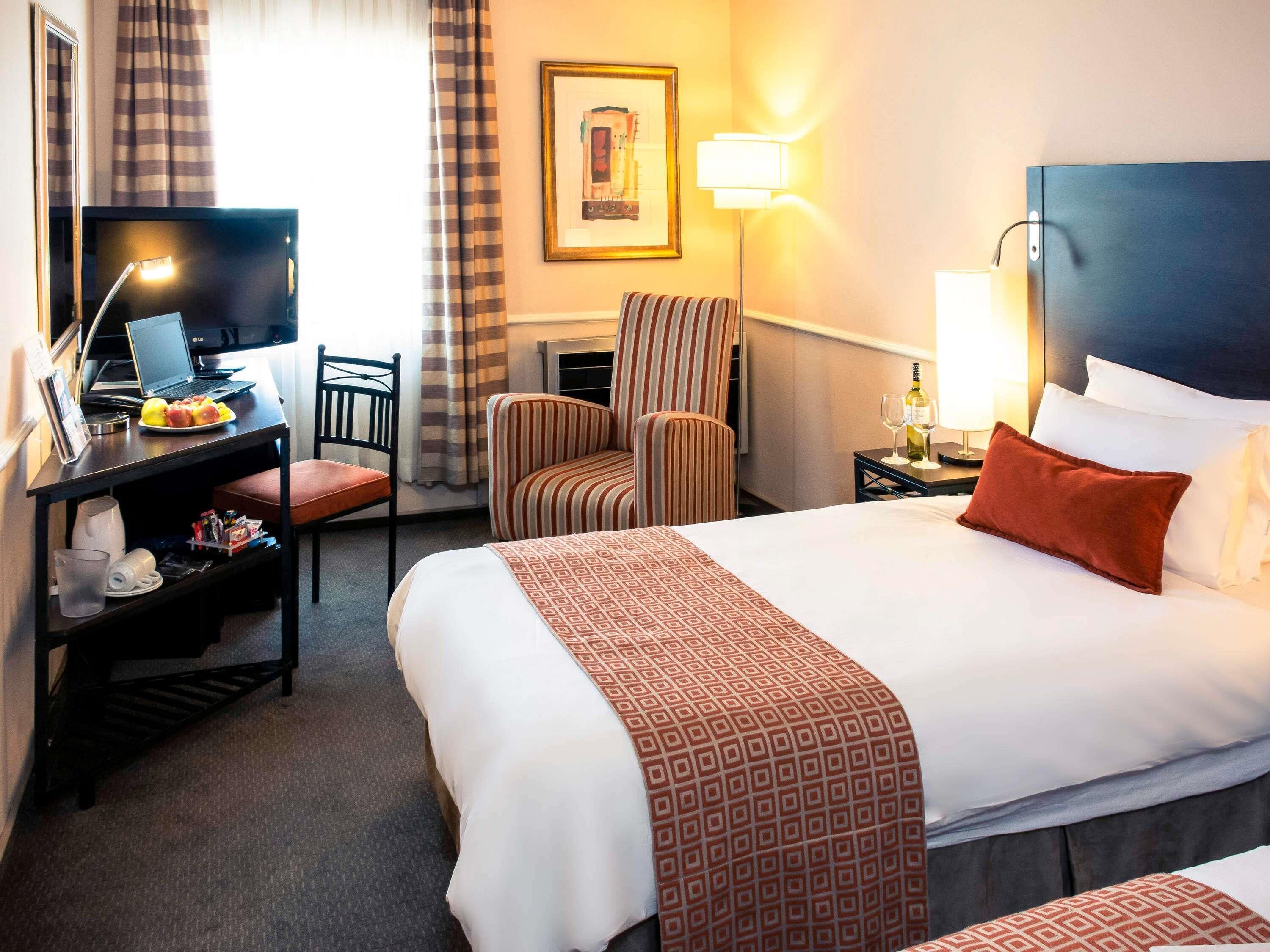 Habitación de hotel con una cama, un escritorio con una computadora portátil, una silla y una lámpara.