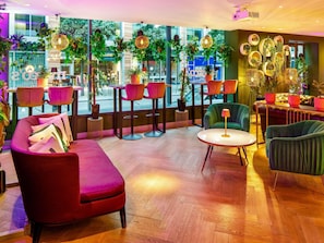 A modern lounge area with a sofa, chairs, a round table, and potted plants.