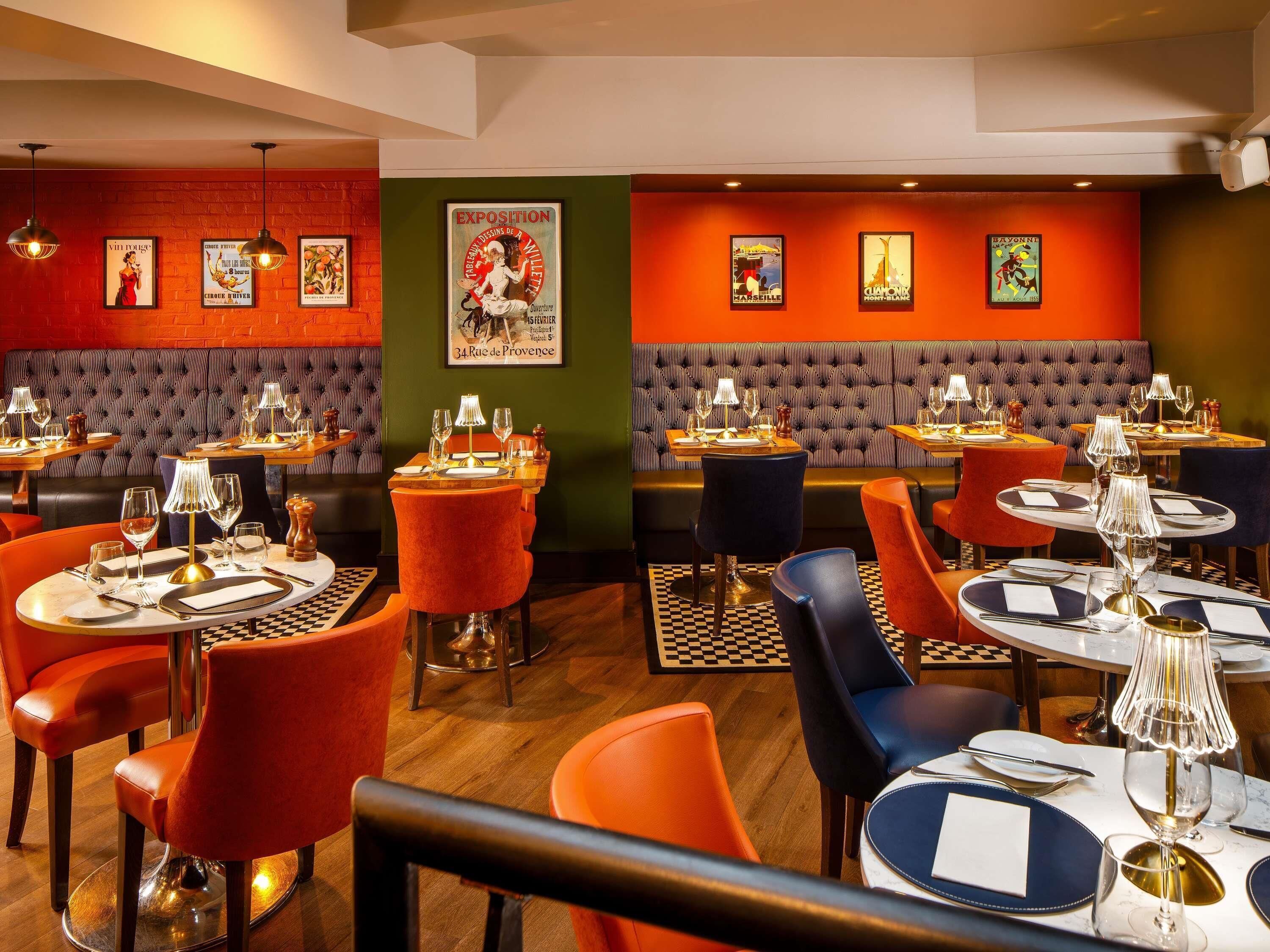 En restaurantindretning med runde borde, røde og blå stole samt et skakternet gulv.