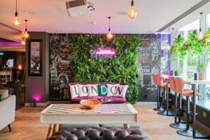 A modern interior with a green wall, a neon sign, and a seating area with a table and chairs. - Mercure London Bankside (London)