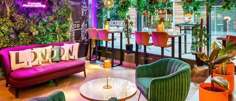 A modern lounge area with a vibrant green sofa, a round glass table, and a bar area with pink chairs.