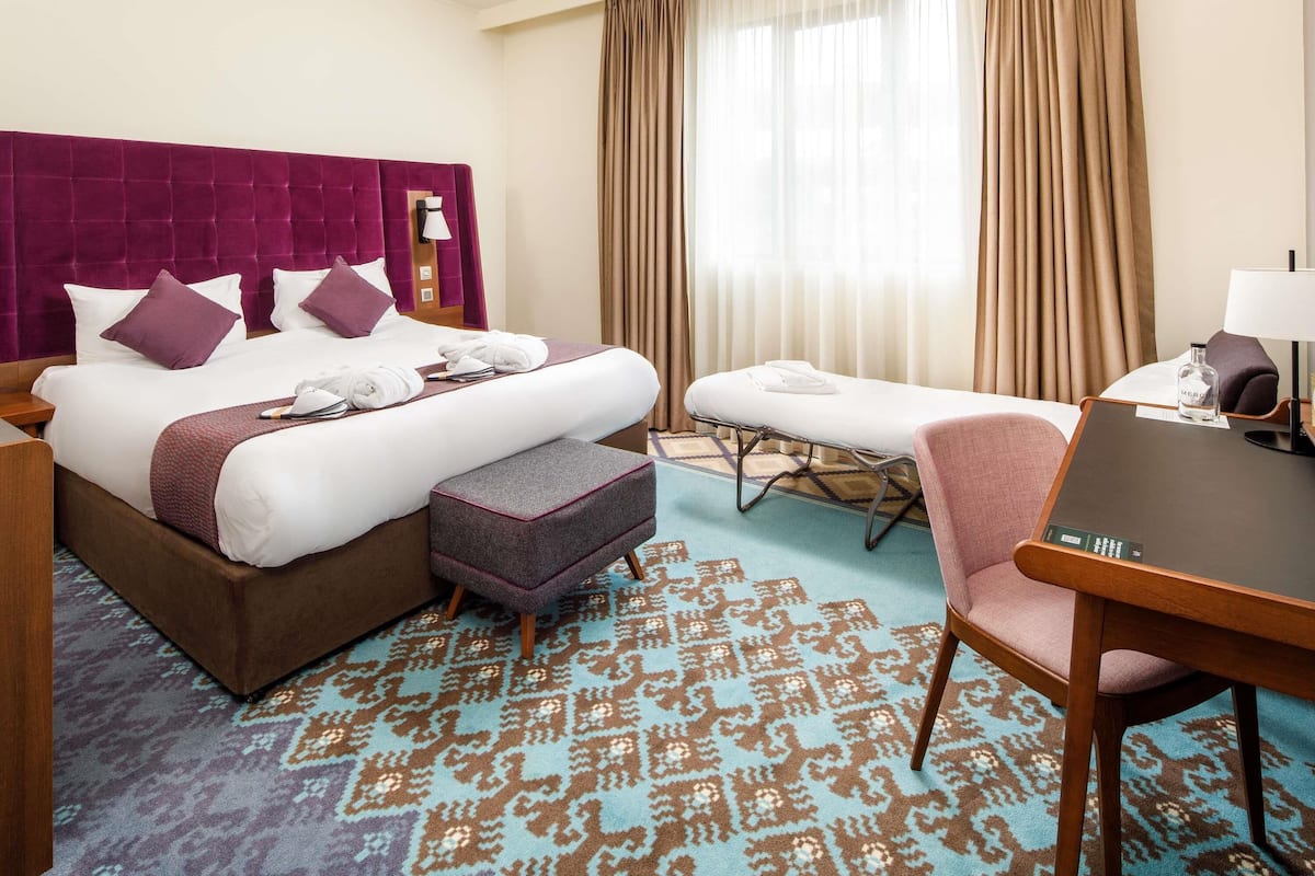 A hotel room with a large bed, a desk, a chair, and a massage table.
