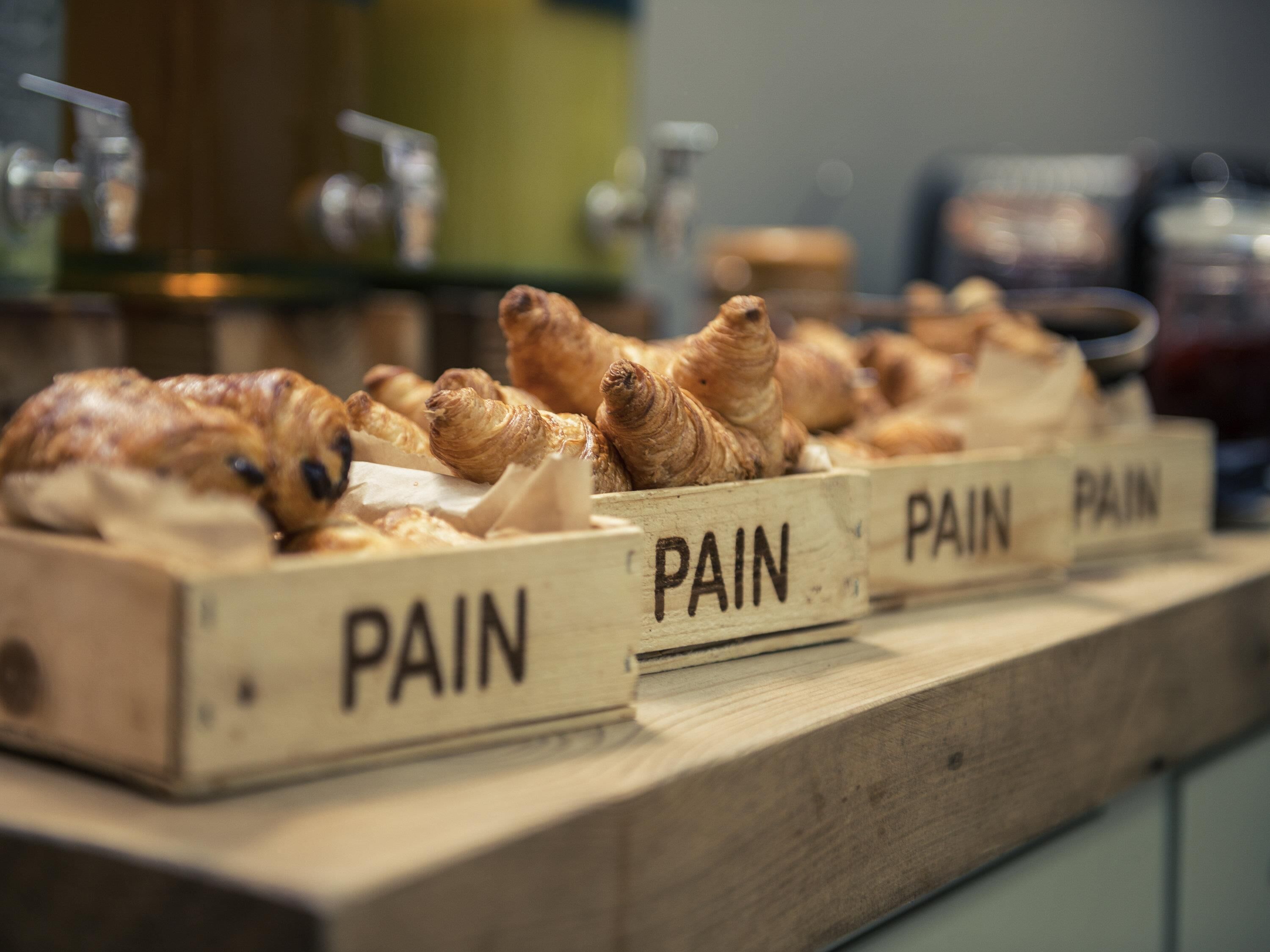 Cajas de madera con la etiqueta 'PAIN' que contienen pasteles sobre una encimera.