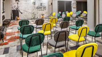Uma sala de conferências com piso xadrez, cadeiras verdes e amarelas, um muro com grafites e uma lareira.