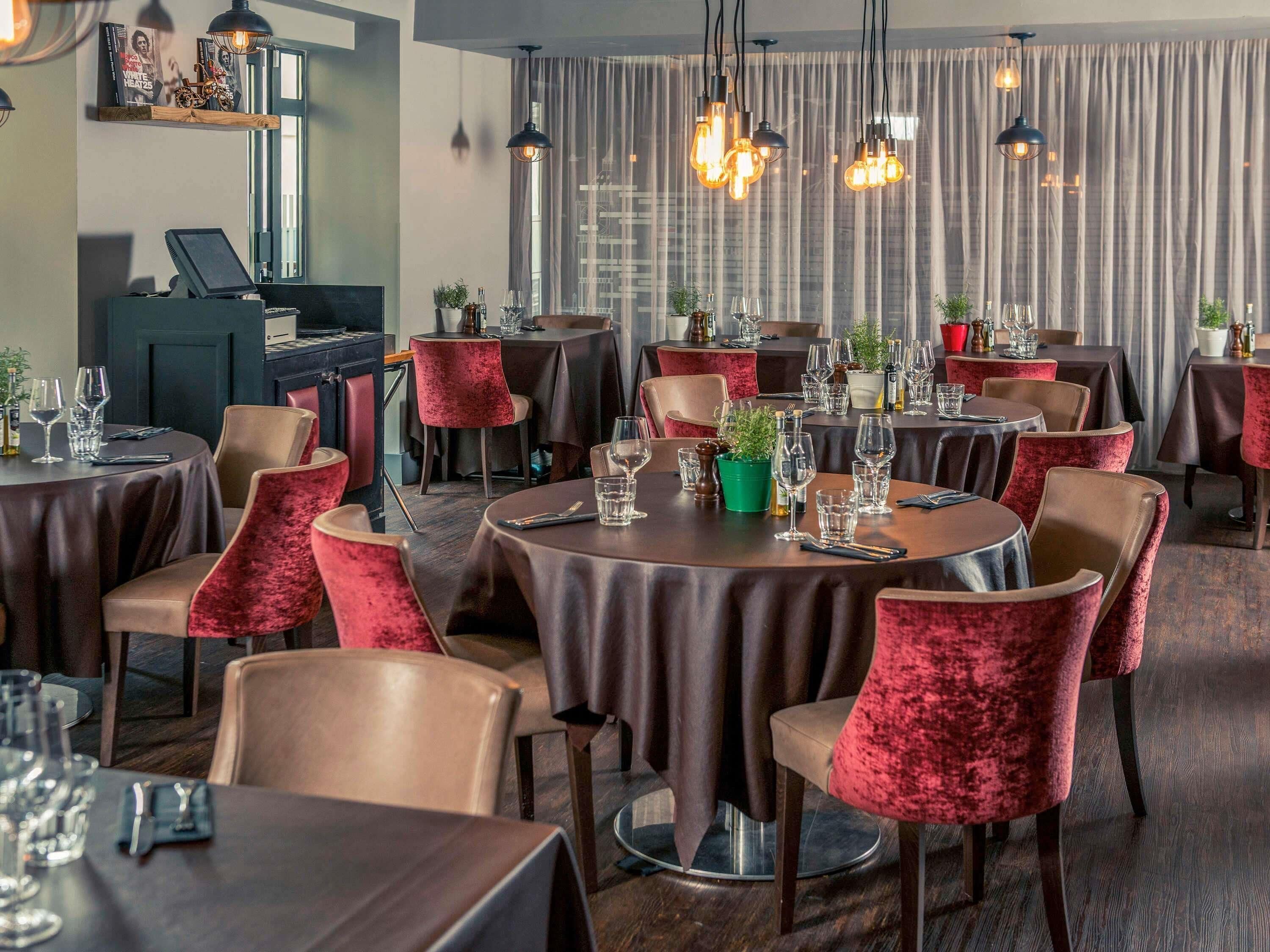 Un restaurante con mesas redondas, sillas de terciopelo rojo y lámparas colgantes.