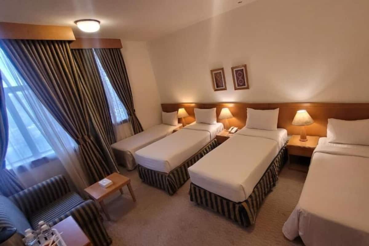 A hotel room with three single beds, a sofa, a small table, and a window with curtains.