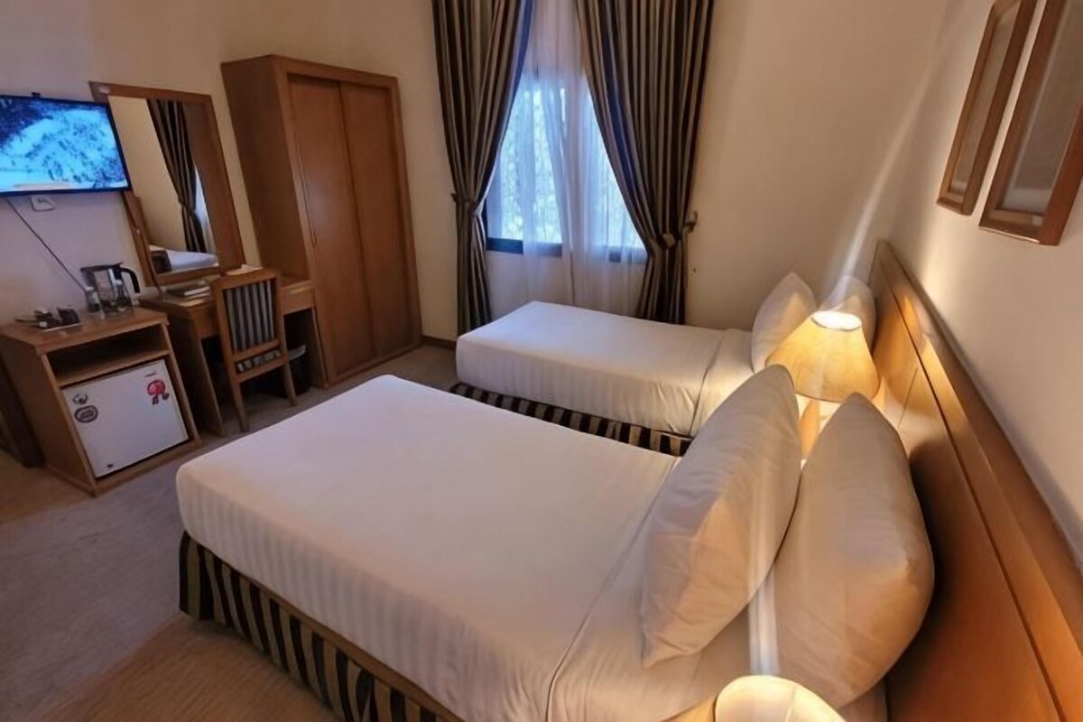 Habitación de hotel con dos camas, un escritorio con silla, armario, televisor y ventana con cortinas.