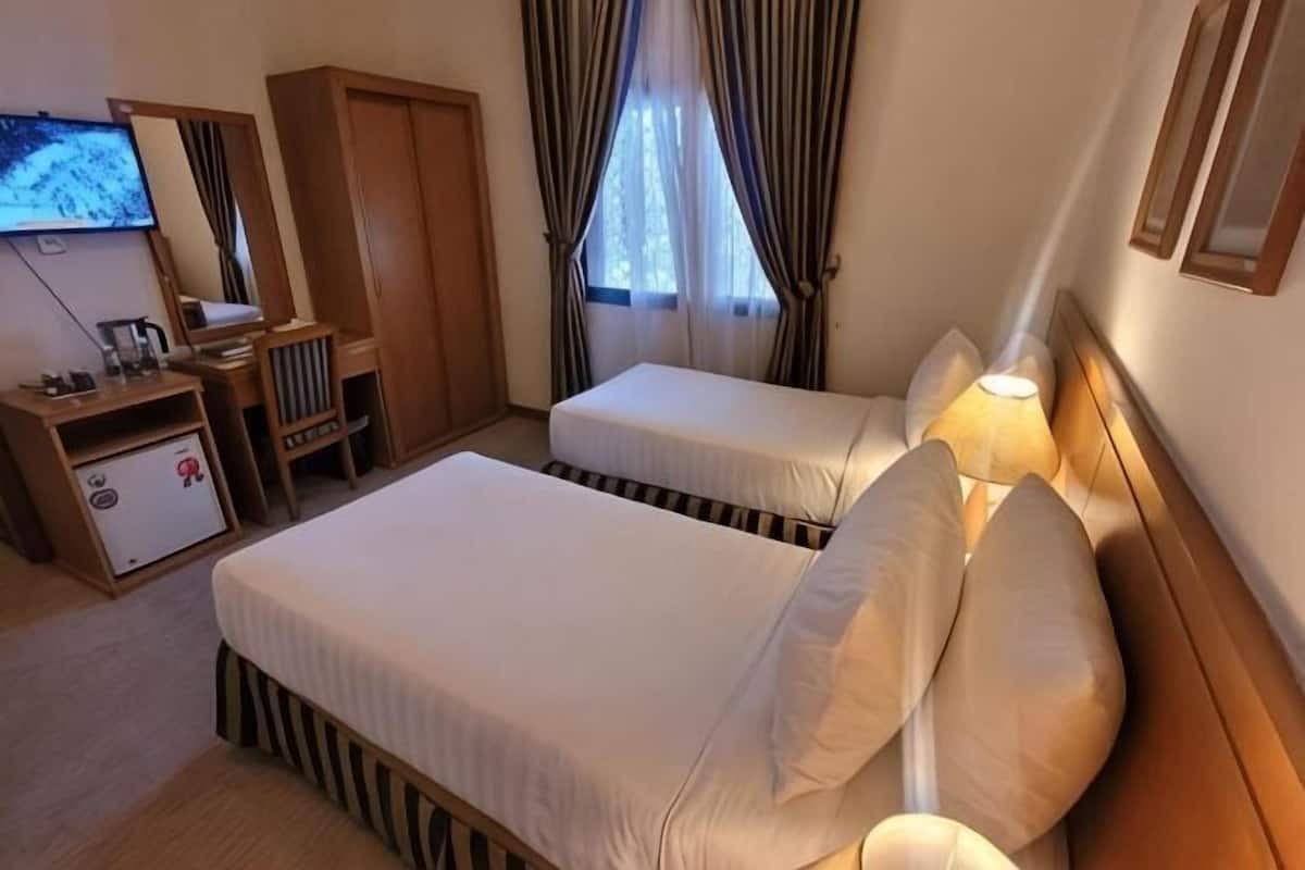 A hotel room with two beds, a desk with a chair, a wardrobe, a television, and a window with curtains.