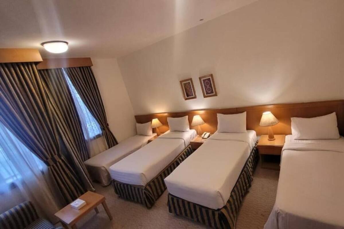 A hotel room with three single beds, a small table, and a chair.