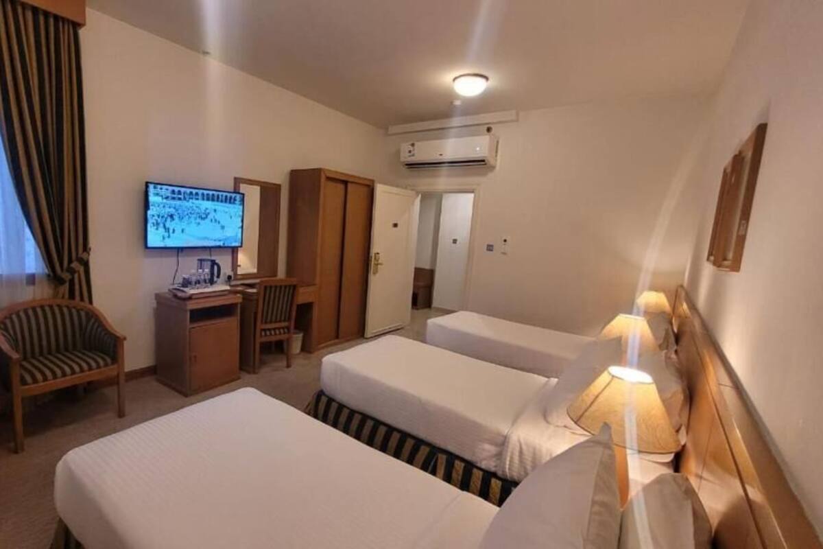 A hotel room with two beds, a desk with a computer, a TV, a wardrobe, and a lamp.