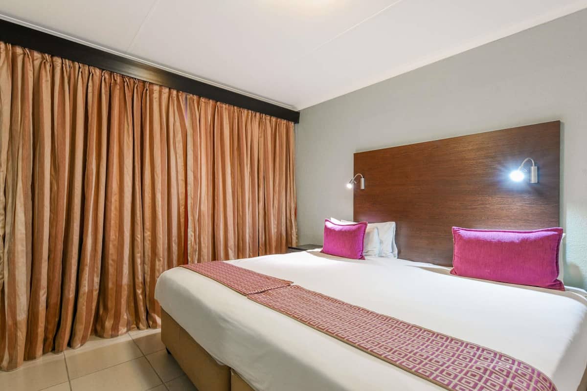 Una habitación de hotel con una cama grande, dos lámparas de noche, un cabecero y una cortina.