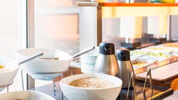 A buffet setup with bowls of food, a coffee maker, and condiments.