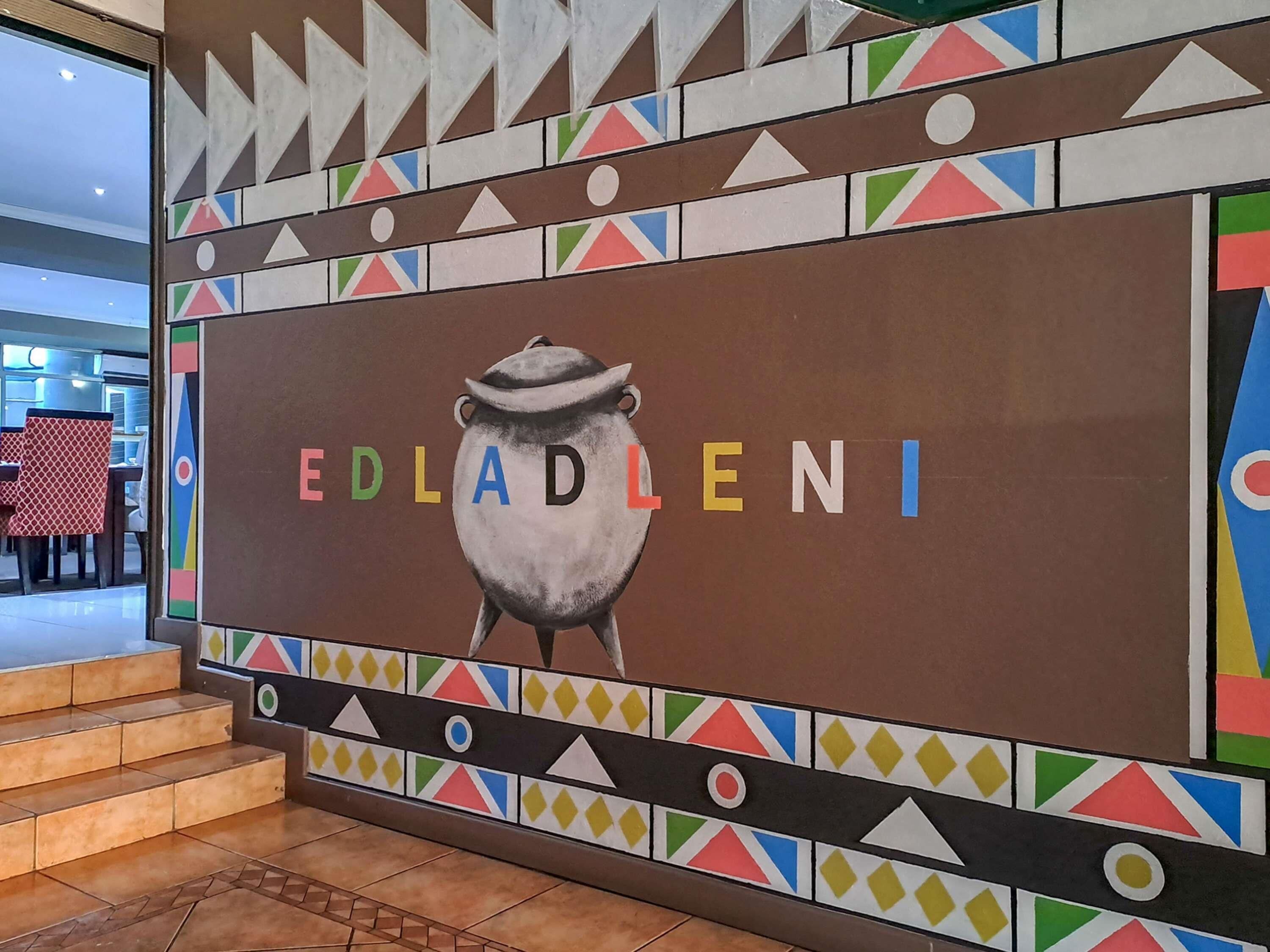 Un mur orné de motifs géométriques colorés, avec le texte « EDLADLENI » inscrit au centre.