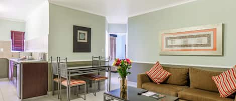 Un salon moderne avec un canapé, une table basse et un coin repas comprenant des chaises, et une cuisine en arrière-plan.