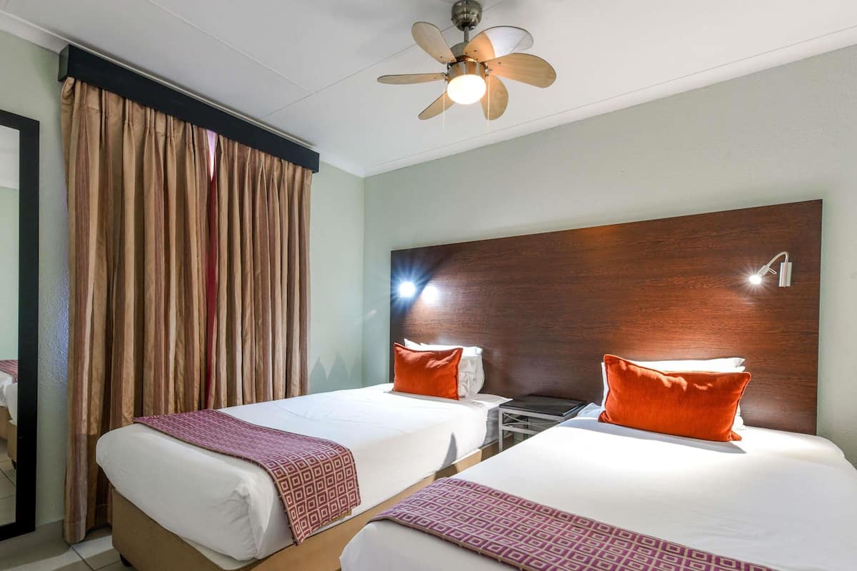 Habitación de hotel con dos camas, un ventilador de techo, una mesita de noche y un espejo grande.