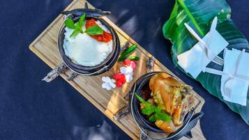 A wooden serving board with two bowls of food, a banana leaf, and a pair of white plastic utensils.