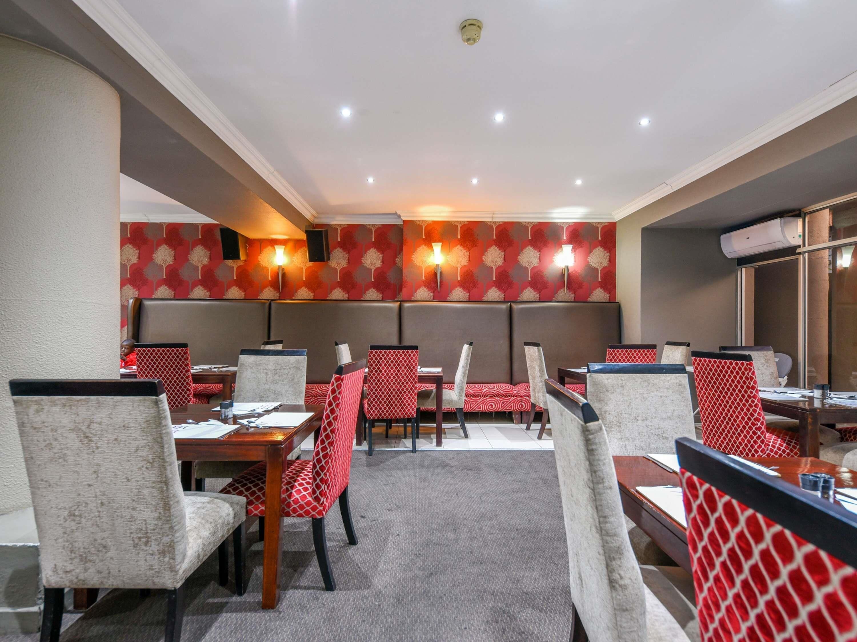 Un restaurante con cabinas y mesas, decoración de pared con un estampado rojo e iluminación empotrada en el techo.