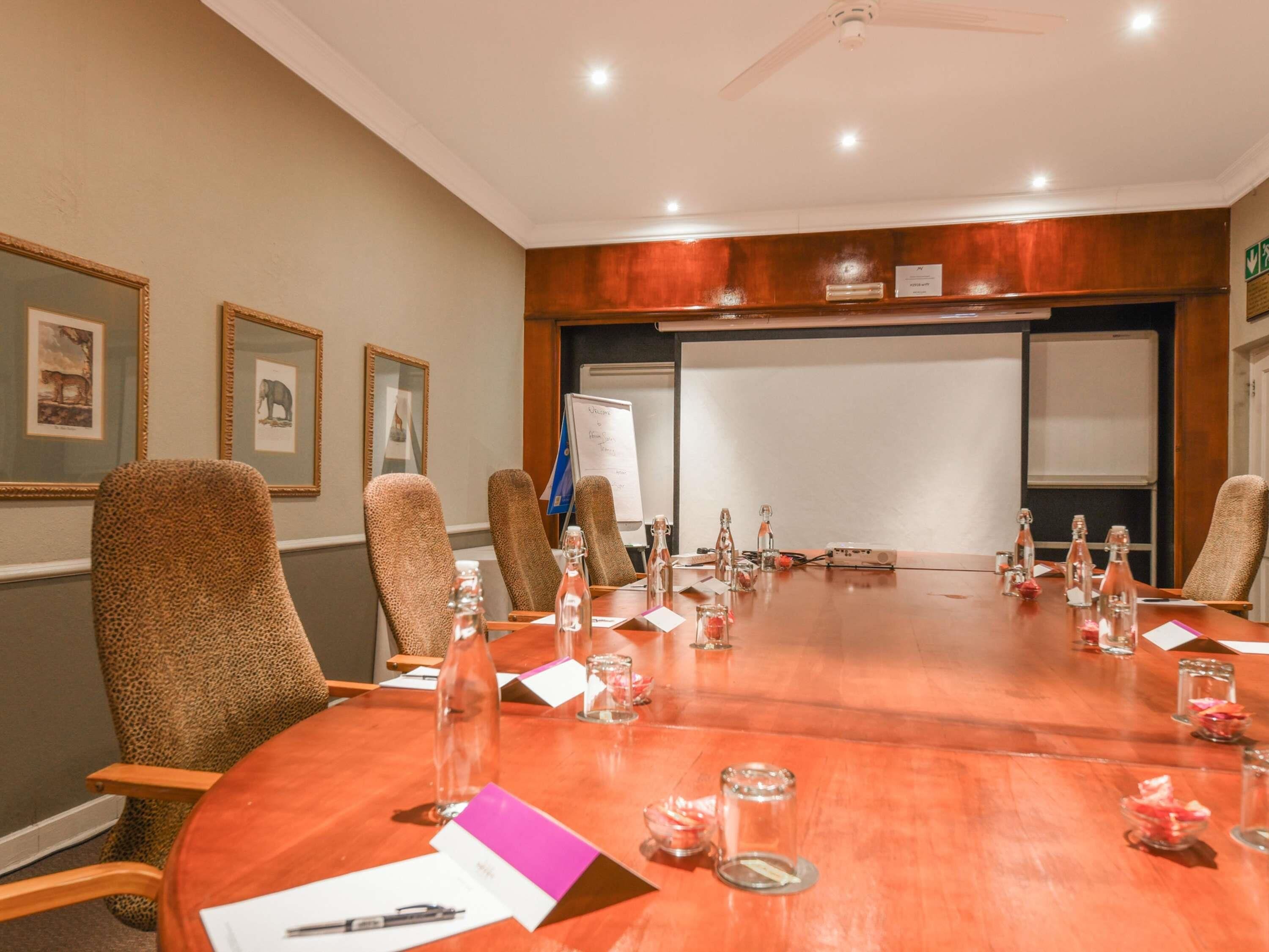 Un salón de conferencias con una gran mesa ovalada, sillas de cuero y una pizarra.