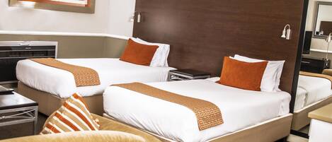 A hotel room with two beds, each with white linens and orange pillows, a wooden headboard, a bedside table, and a chair.