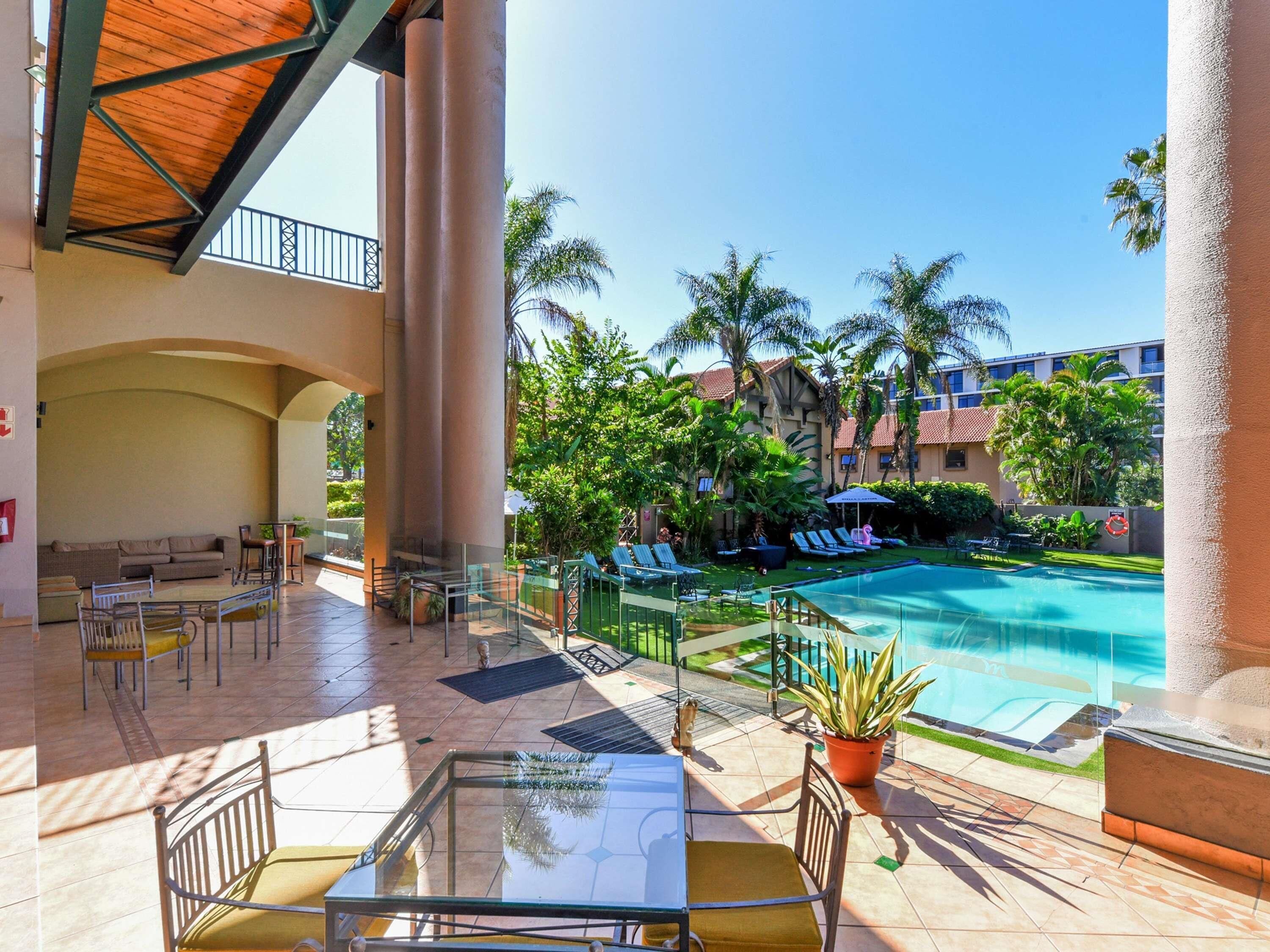 A hotel patio with a pool, lounge chairs, and a glass table.