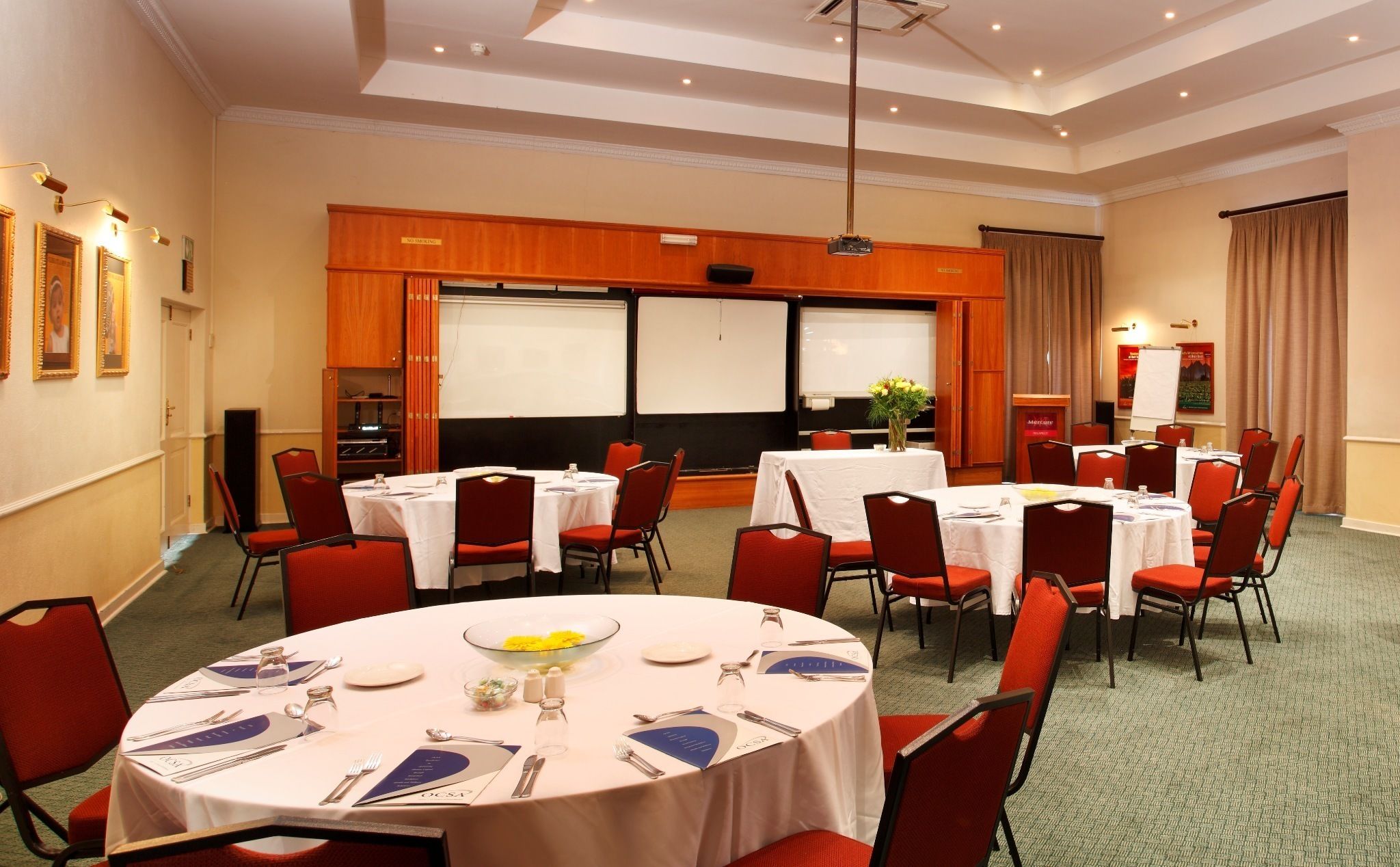 A conference room with multiple tables, red chairs, and a projector screen.
