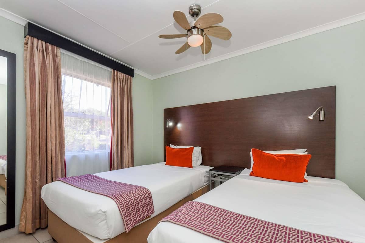 Habitación de hotel con dos camas, ventilador de techo, mesita de noche y ventana con cortinas.