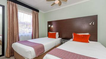 Une chambre d’hôtel avec deux lits, un ventilateur de plafond, une table de chevet et une fenêtre avec des rideaux.